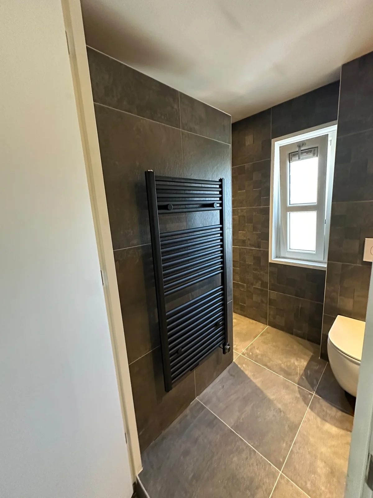 Zwarte handdoekradiator en wandcloset in de moderne badkamer na renovatie
