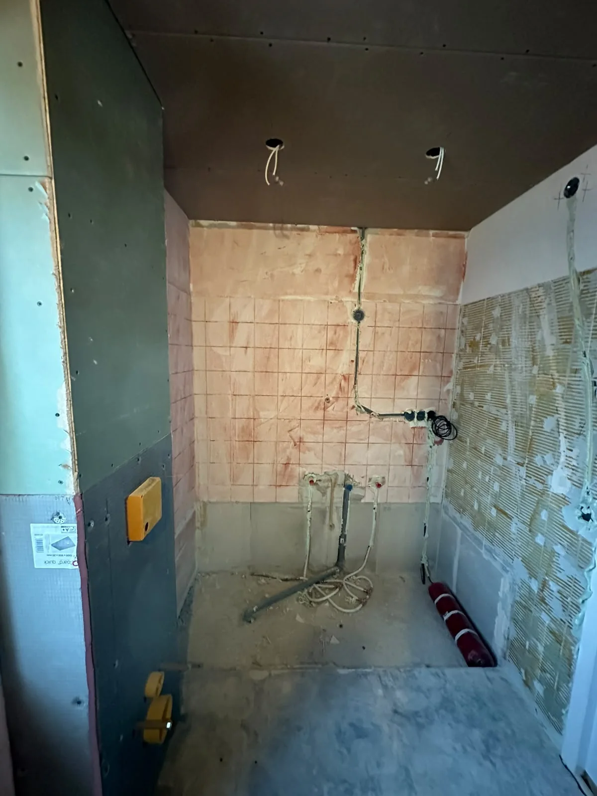 Badkamer voor de renovatie met open leidingen en verwijderde tegels